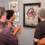 Alameda Post - Visitors to Rhythmix Cultural Works gather around an artwork of an entangled bird and serpent.