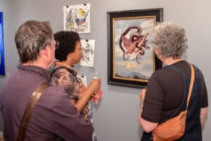 Alameda Post - Visitors to Rhythmix Cultural Works gather around an artwork of an entangled bird and serpent.