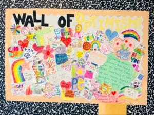 Alameda Post - A colorful decorated bulletin board labeled "Wall of Optimism" with lots of brightly colored encouraging messages.