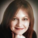 Alameda Post - A headshot of a woman with brown hair, wearing a black shirt. She is smiling.