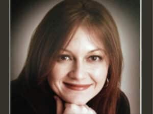 Alameda Post - A headshot of a woman with brown hair, wearing a black shirt. She is smiling.