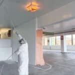 Alameda Post - A person in P.P.E. sprays paint onto the ceiling of a parking garage.