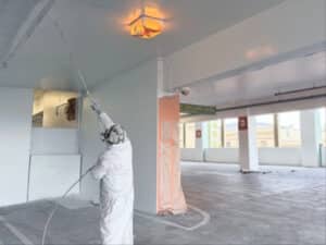 Alameda Post - A person in P.P.E. sprays paint onto the ceiling of a parking garage.
