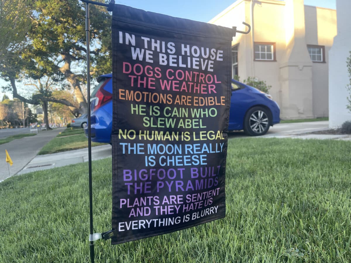 Alameda Post - A sign in someone's yard that says "In this house we believe dogs control the weather, emotions are edible, he is cain who slew abel, no human is legal, the moon really is cheese, beg foot built the pyramids, plants are sentient and they hate us, and everything is blurry."
