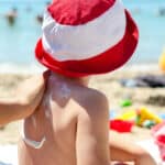 Alameda Post - An adult applies sunscreen to a child's back on a beach.