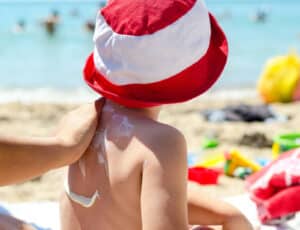 Alameda Post - An adult applies sunscreen to a child's back on a beach.