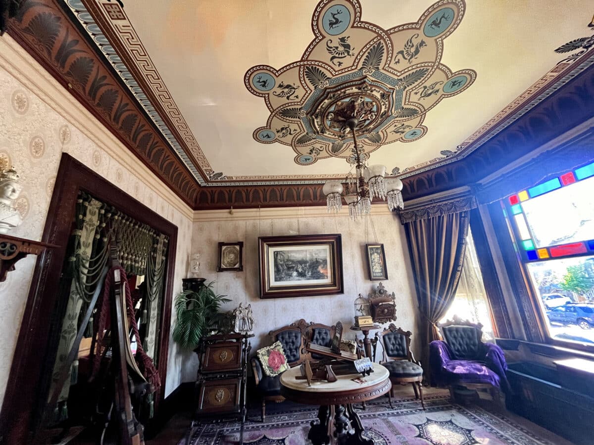 Alameda Post - A rich front room that appears frozen in time in the Victorian era style. Everything is richly decorated with cloth, wood, and art.