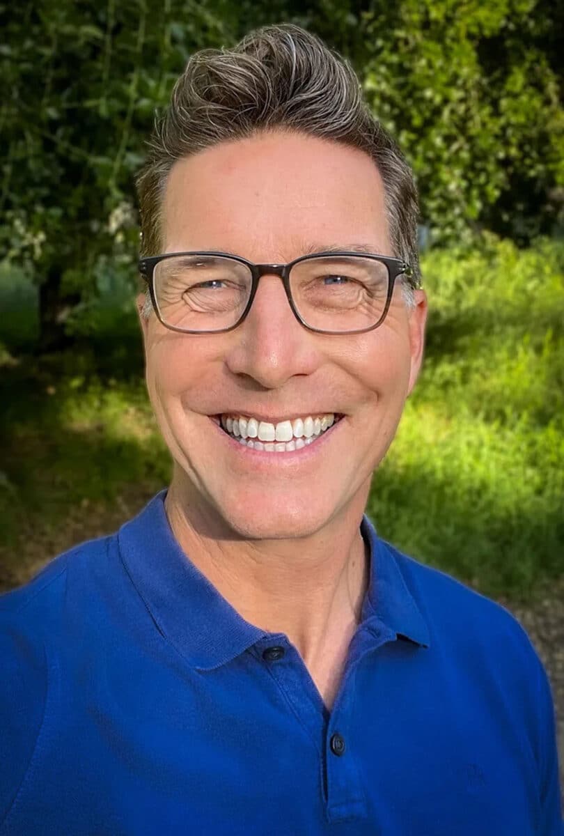 Alameda Post - A man with a broad smile and glasses smiles at the camera. 
