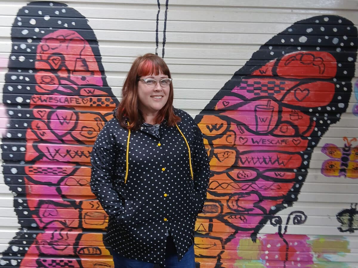 Alameda Post - a woman stands in front of a butterfly mural