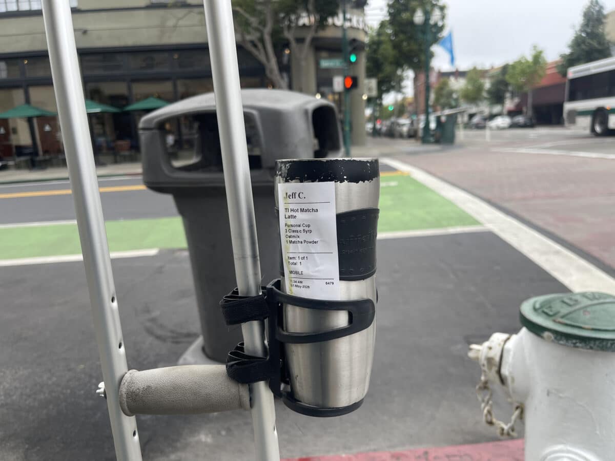Alameda Post - A reusable coffee cup with a starbucks sticker on it, resting in a cup holder on a crutch. 
