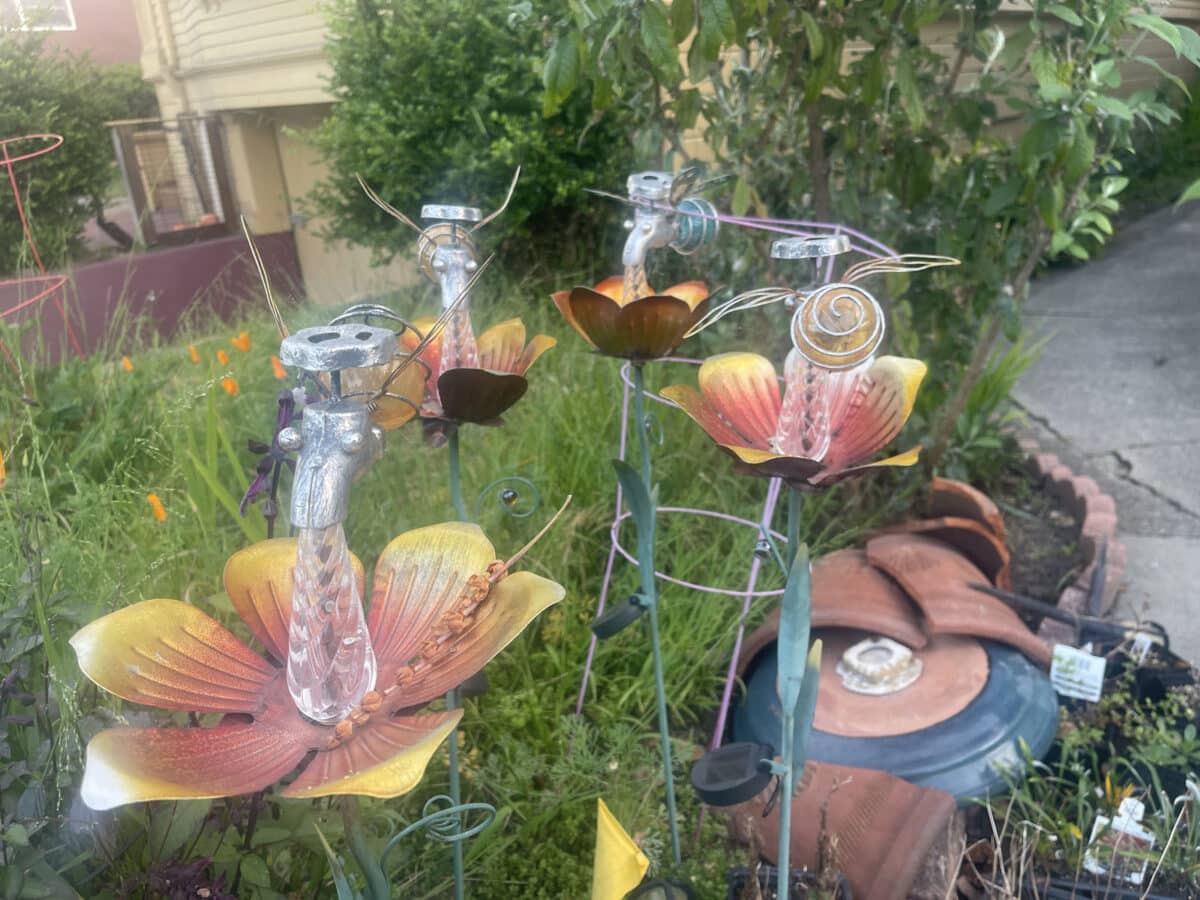 Alameda Post - a metal sculpture of flowers and pollinators in a yard.
