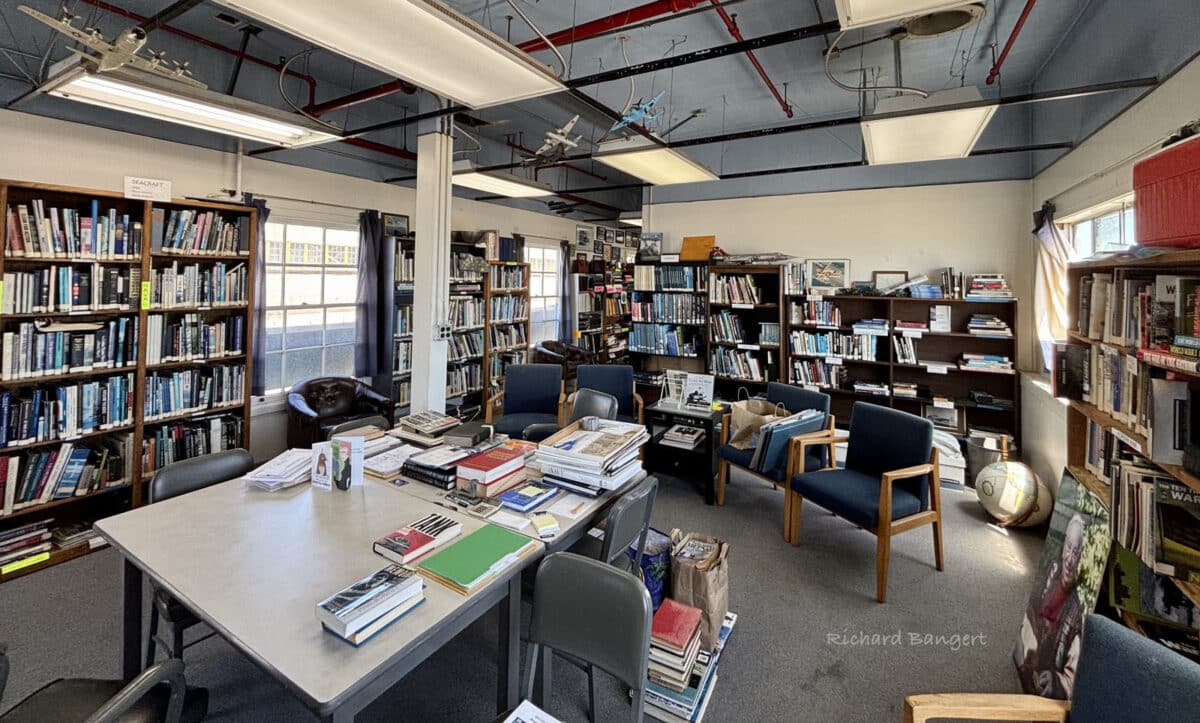 Alameda Post - A room full of overflowing bookshelves, a table, and chairs.