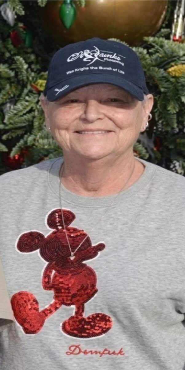 Alameda Post - Barbara Jane Kettelhut smiles in front of a Christmas tree wearing a baseball hat and Mickey Mouse sweatshirt.