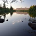 Alameda Post - A beautiful, reflective lake with mountains and trees in the background.