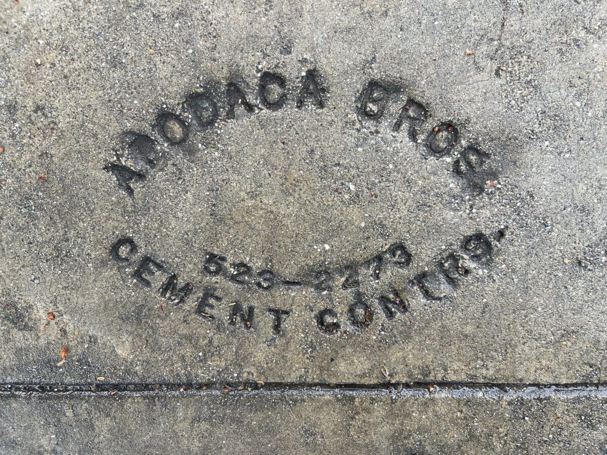 Alameda Post - A stamped sidewalk brand with a phone number.