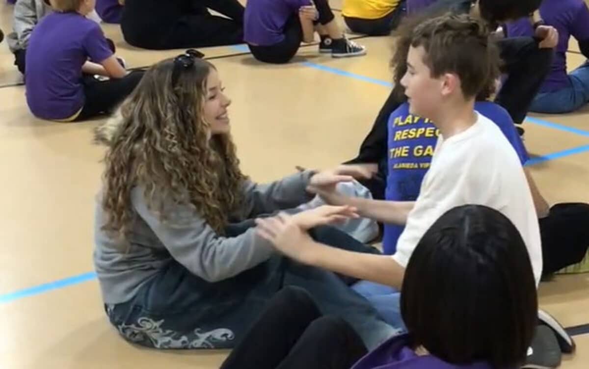 Alameda Post - A young woman and a boy sit on the gym floor together and smile while sitting across from one another.