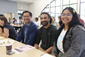 Alameda Post - Three teachers in a room full of A.U.S.D. teachers smile at the camera.