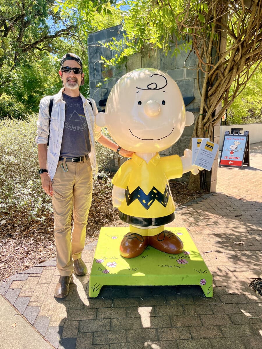 Alameda Post - A man smiles next to a large statue of Charlie Brown.