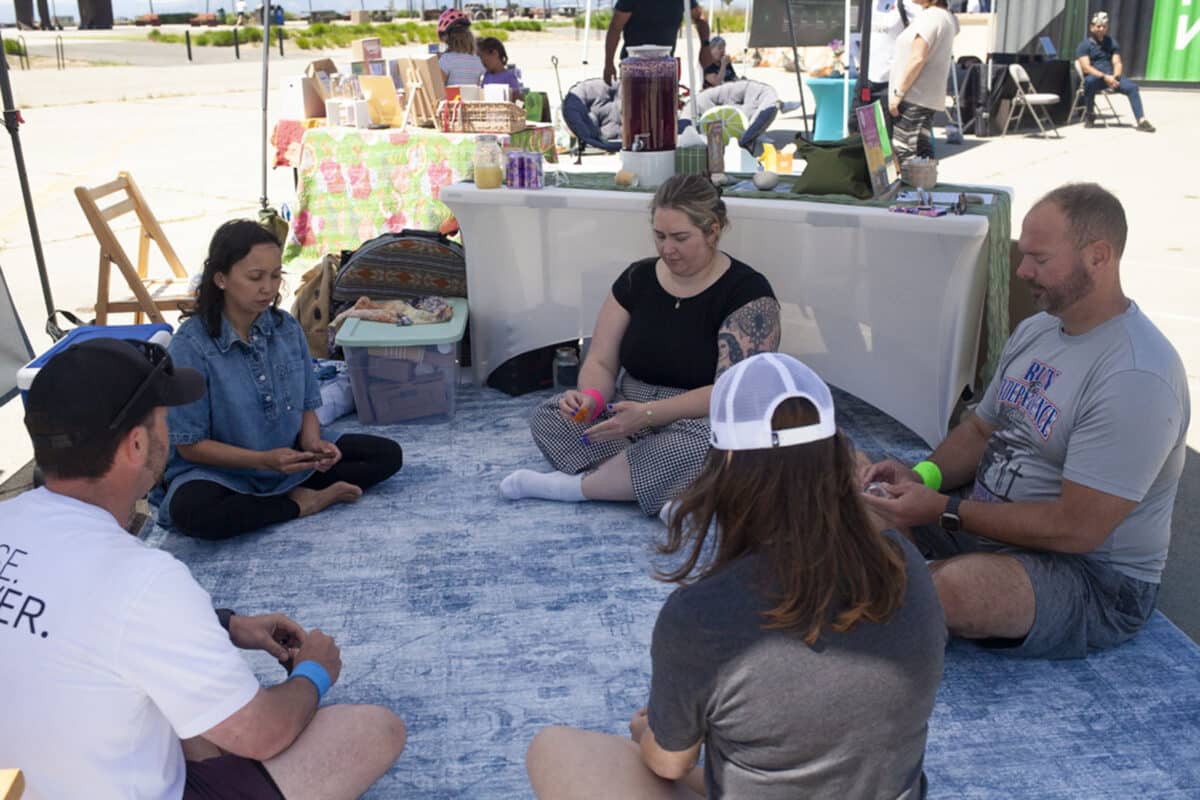 Alameda Post - A small group of five people sit in a circle on a blanket beneath a booth tent.