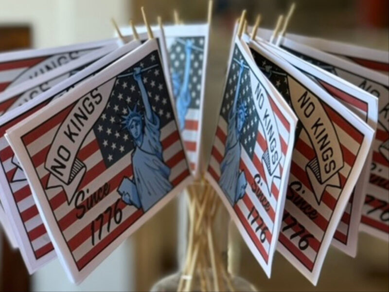 Alameda Post - A jar of small handheld flags. They are the American flag and have the statue of liberty on them and say No Kings Since 1776.