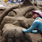 Alameda Post - A photo of a smiling contestant next to a sand sculpture of an animal.