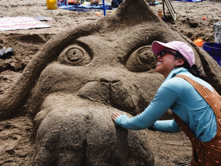 Alameda Post - A photo of a smiling contestant next to a sand sculpture of an animal.