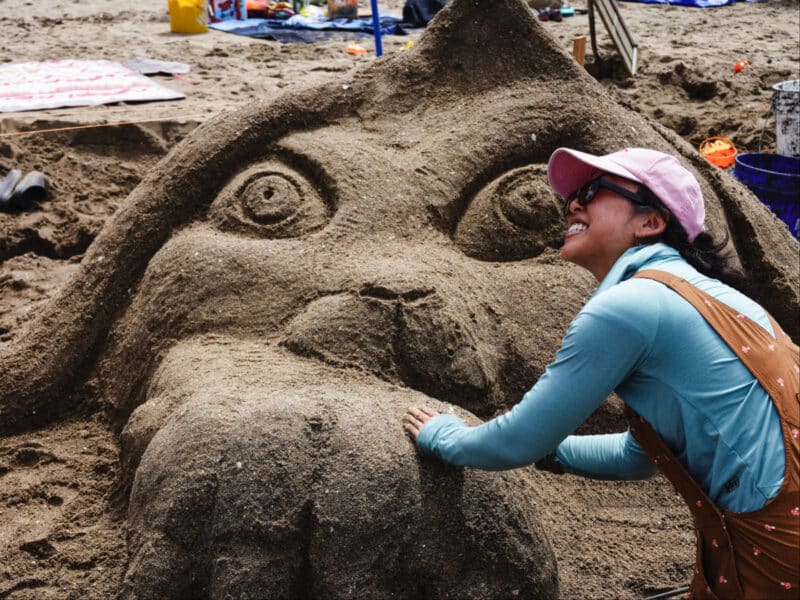 Alameda Post - A photo of a smiling contestant next to a sand sculpture of an animal.