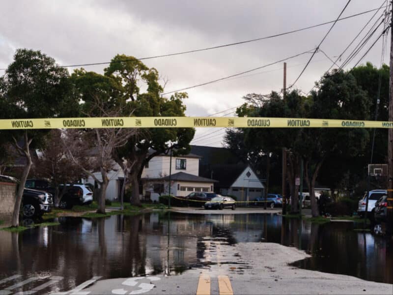 Alameda Post - A piece of caution tape across an intersection. Flooding on an Alameda street is visible in the background