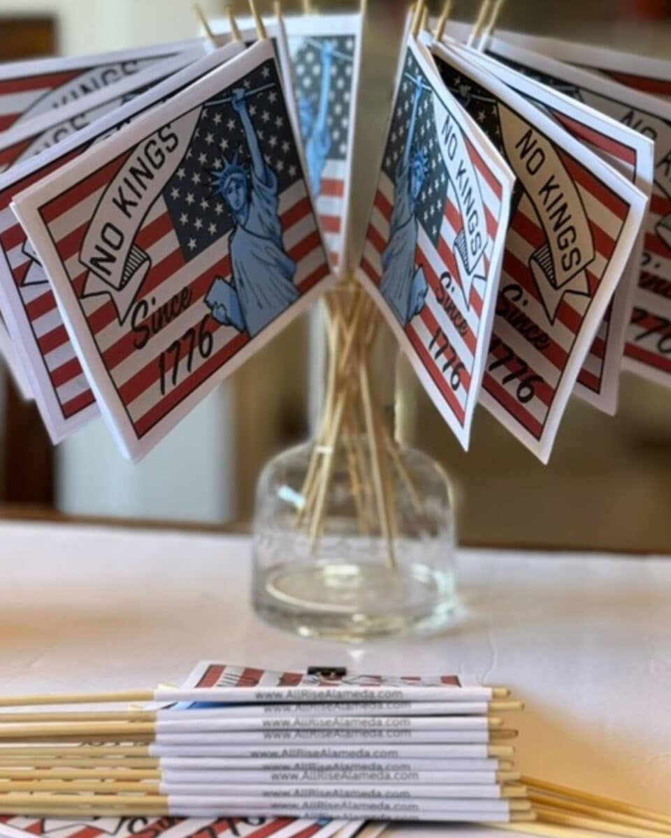 Alameda Post - A jar of small handheld flags. They are the American flag and have the statue of liberty on them and say No Kings Since 1776.