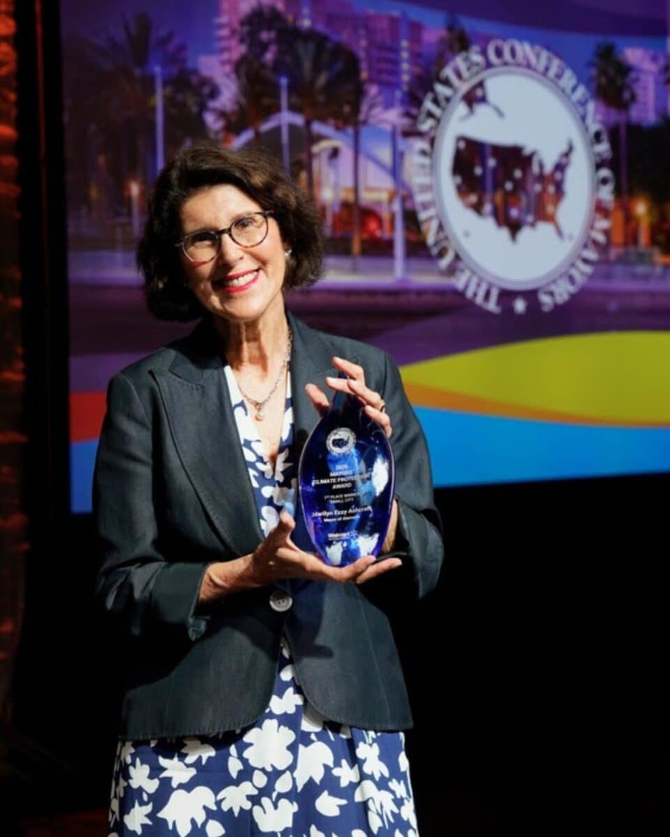 Alameda Post - Marilyn Ezzy Ashraft smiles and holds a glass sculpture, the 2026 Mayors’ Climate Protection Award.