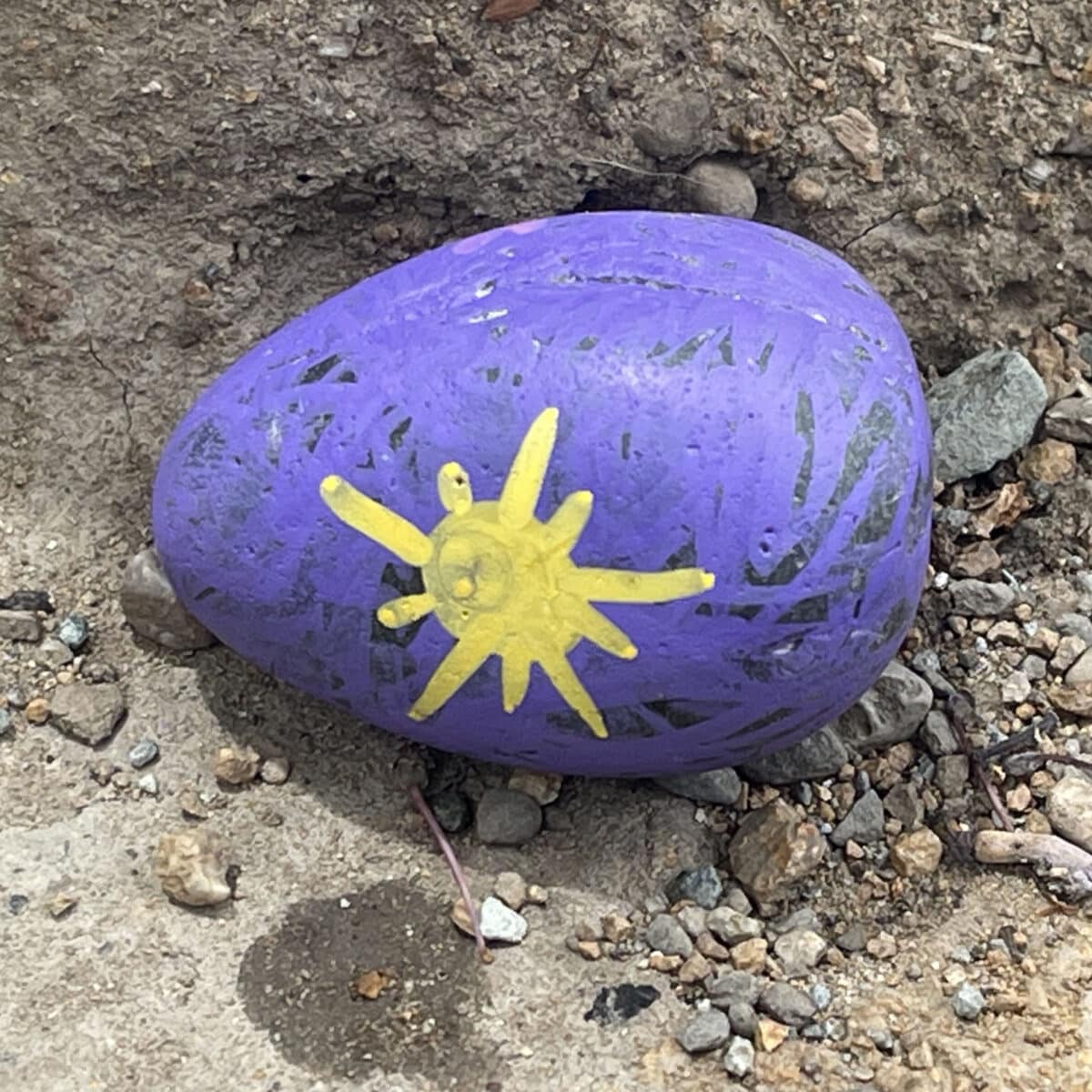 Alameda Post - A stone on the ground painted with purple paint and a yellow sun. 