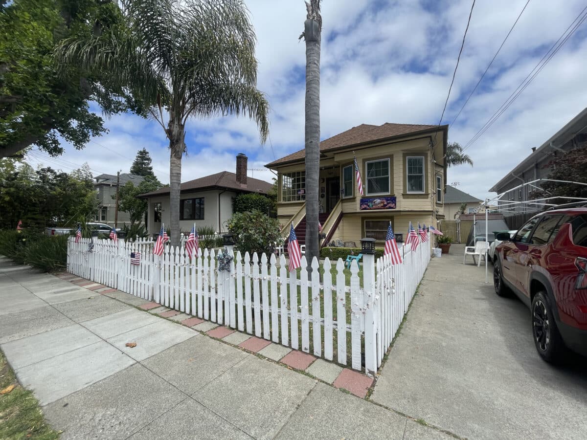 Alameda Post - A home with a white picket fence. The fence has small American flags placed every six feet or so. 