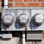Alameda Post - Three side by side electricity meters on a brick wall.