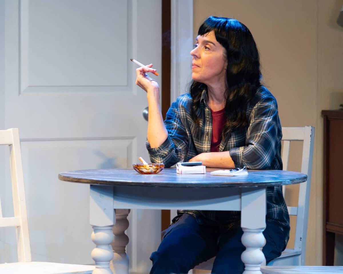 Alameda post - A woman sits at a kitchen table with a cigarette. 