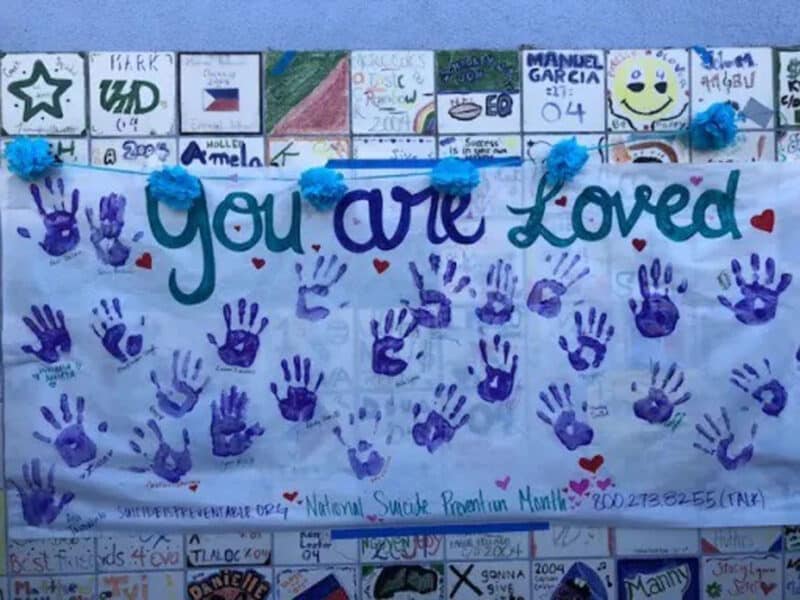 Alameda Post - A handmade poster with handprints that says "You are loved" and has the national suicide prevention phone number.