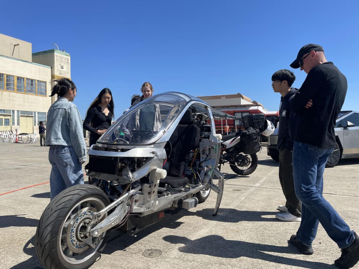 Alameda Post - Visitors gather around a futuristic looking single person vehicle. 