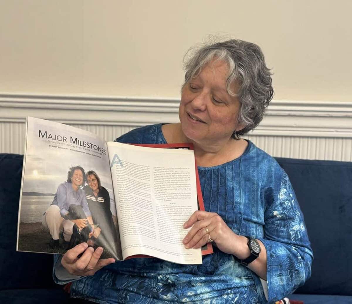 Alameda Post - A woman sitting on a couch holds open a magazine. In the magazine is a photo of her and another woman with the headline "Major Milestone."