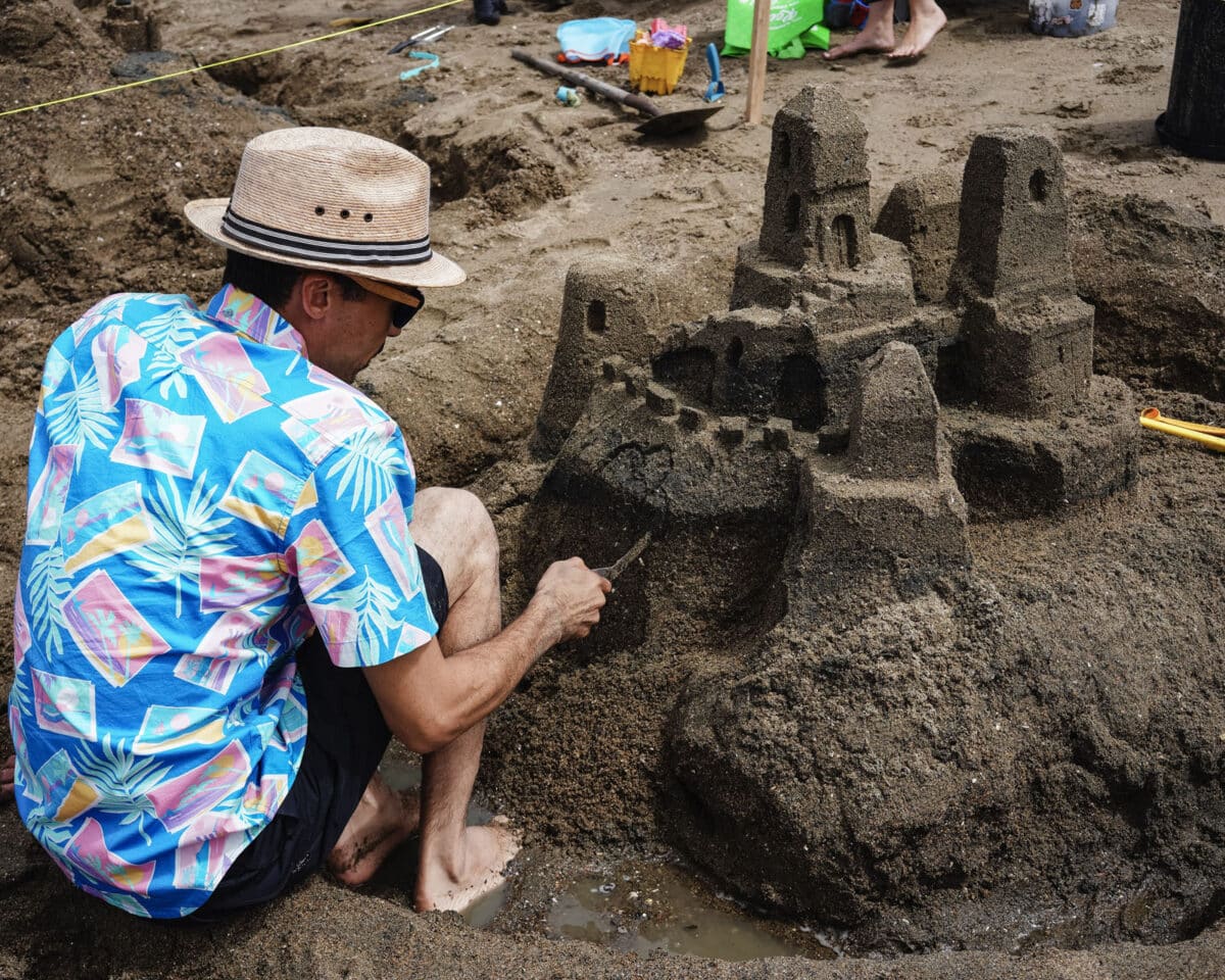 Alameda Post - A man in a Hawaiian shirt and a hat makes a sand castle. 