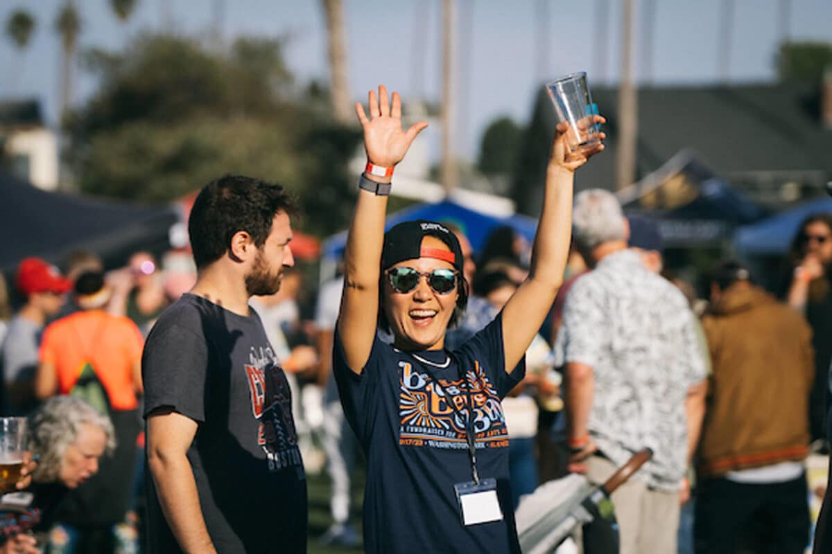Alameda Post, A woman holds an empty beer glass, wearing a Blues Brews and B.B.Q. shirt, and smiles at a festival with her hands in the air.