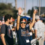 Alameda Post, A woman holds an empty beer glass, wearing a Blues Brews and B.B.Q. shirt, and smiles at a festival with her hands in the air.
