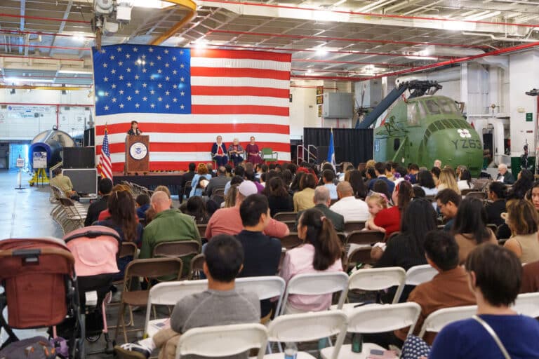 Alameda Post - A crowd of people is seated at a ceremony on the USS Hornet.