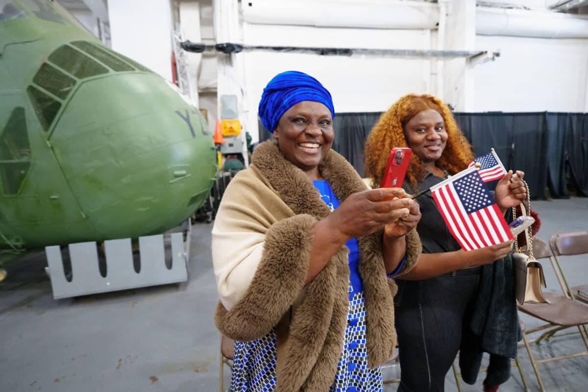 Alameda Post - Attendees of the USS Hornet's naturalization ceremony smile at the camera and hold American flags.