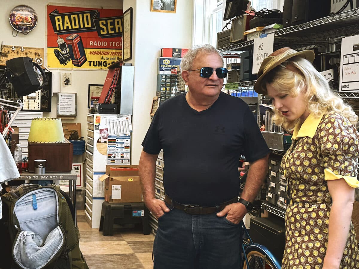 Alameda Post - A woman in vintage clothing and a man look around inside of the California Historical Radio Society.