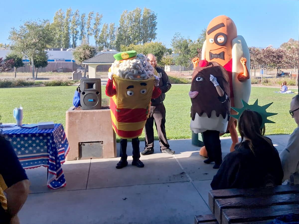 Alameda Post - People in costumes of popcorn, a hotdog, and an ice cream sundae celebrate at the front of a pavillion at Jean Sweeney Open Space Park.