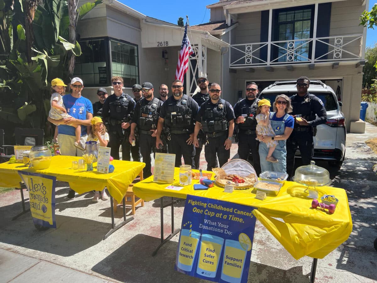 Alameda Post - A family with three young girls stands behind a lemonade stand with ten Alameda Police officers. 