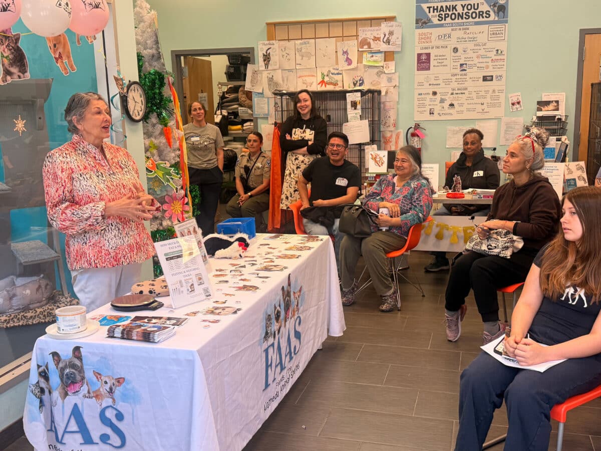 Alameda Post - A woman stands at the front of a room at an F.A.A.S. desk and teaches attendees. 