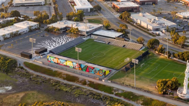 Alameda Post - A render of an Oakland Roots soccer stadium with bleachers and lights.