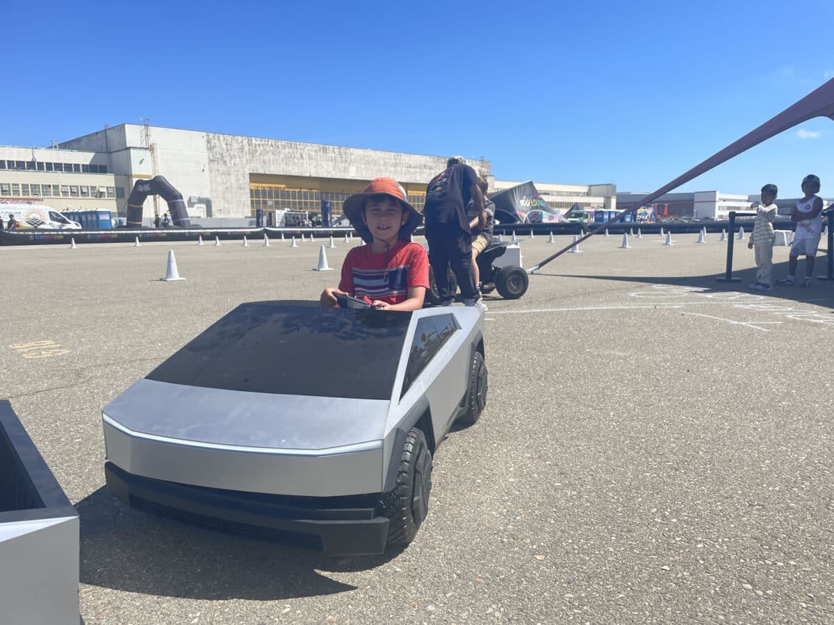 Alameda Post - A young festival attendee sits behind the wheel in a miniature car.