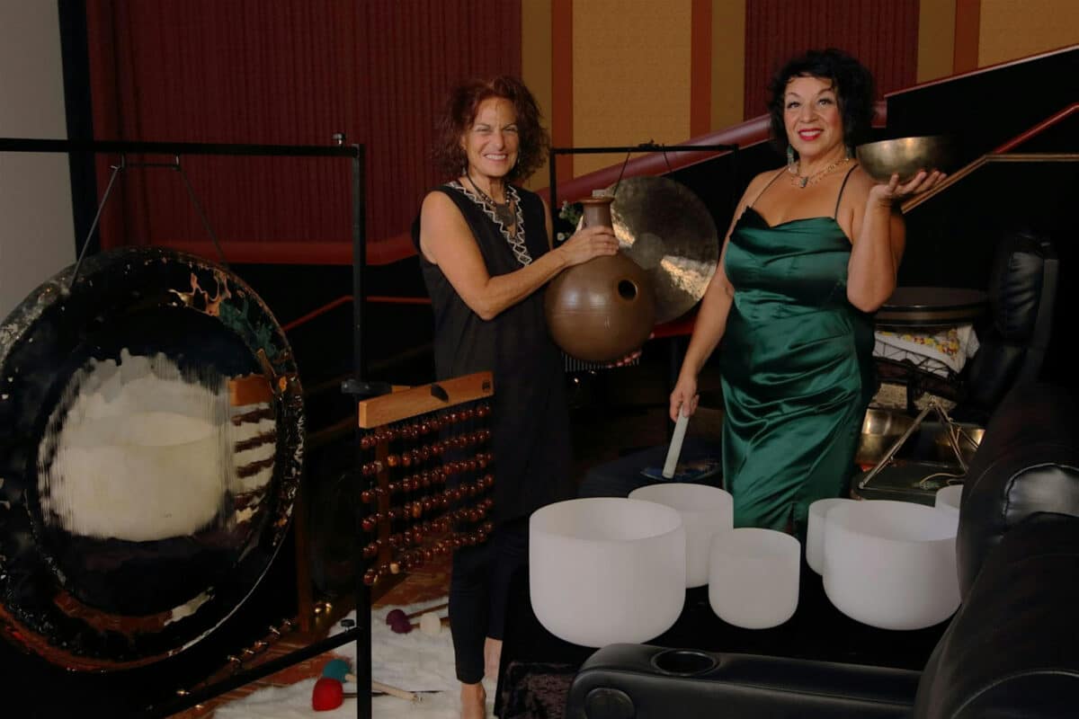 Alameda Post - Two women smile and stand next to various sound bath instuments.