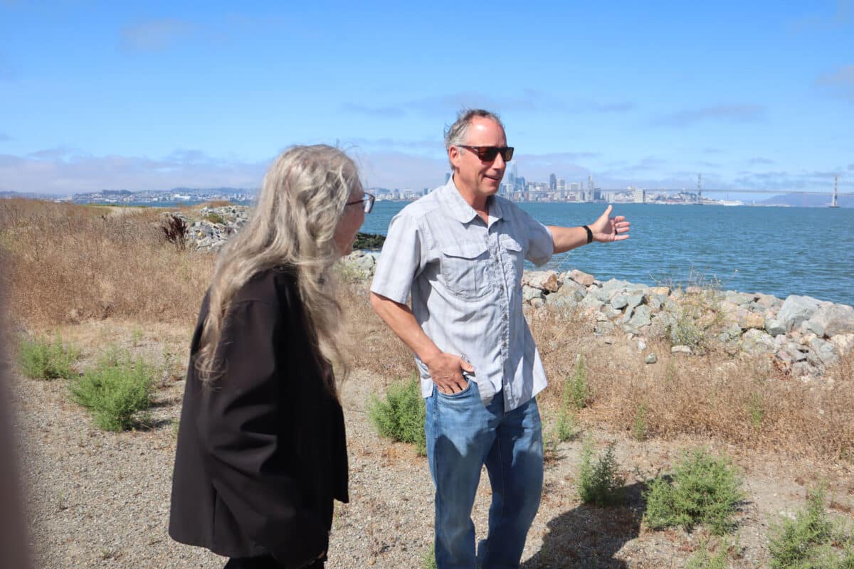 Alameda Post - An environmental engineer speaks to a visitor at Alameda Point, gesturing towards the Bay and the City. 
